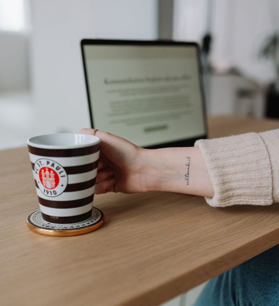 Hand mit Kaffeetasse vor Laptop im Alltag